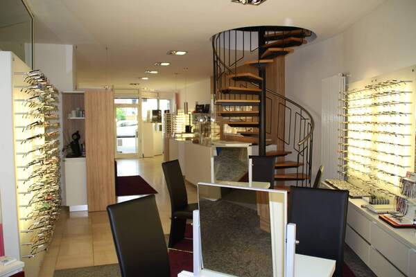 Modernes Optiker-Geschäft mit Brillenauswahl, Beratungstischen und Wendeltreppe.